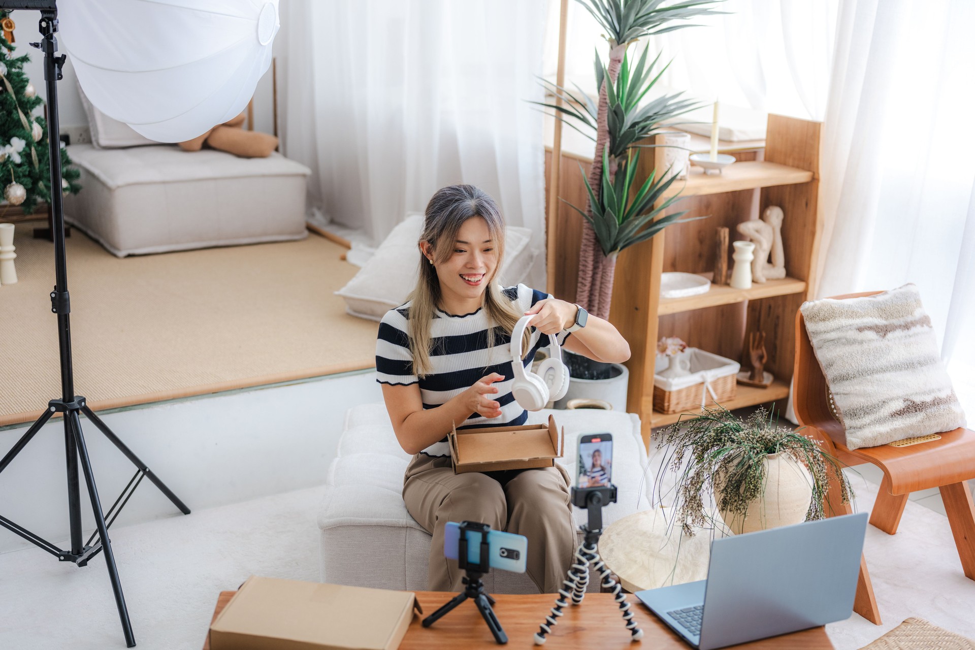 An Asian Chinese female influencer is ready to unbox a headset and record a video with her smartphone while doing so in her living room